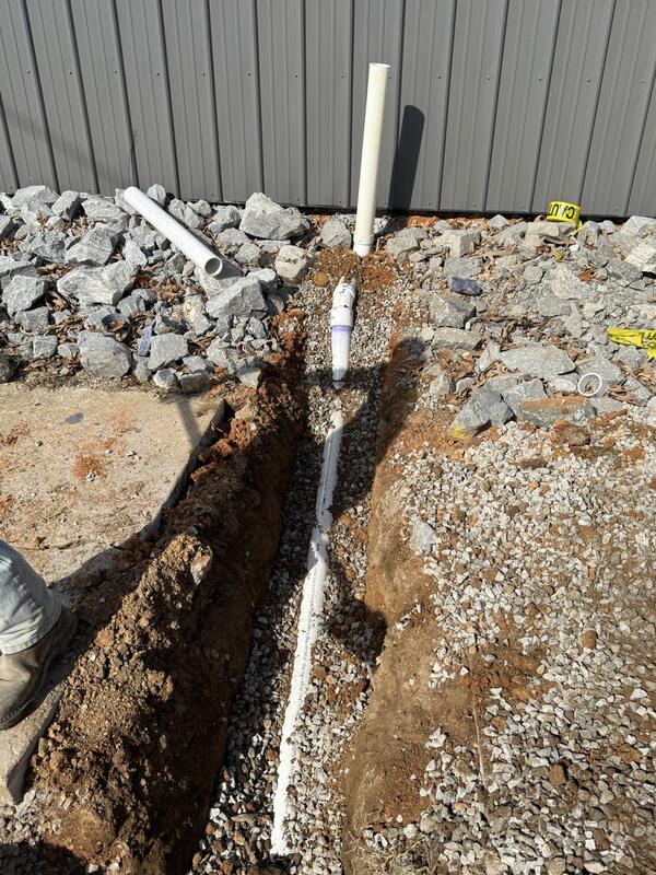 Underground drain line bedded in gravel with a vent riser at a commercial building